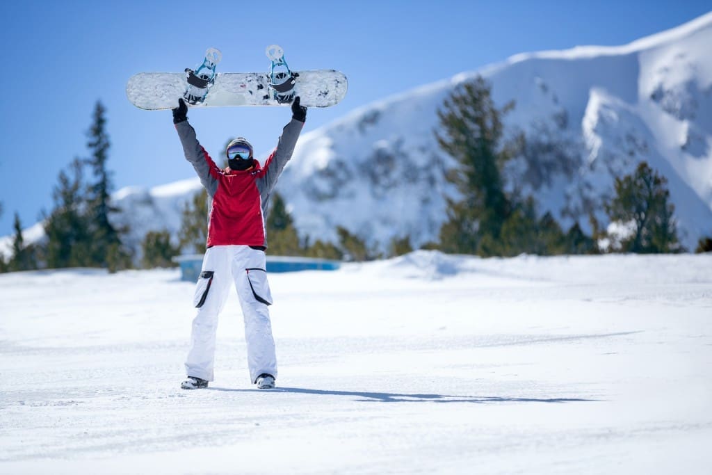 Happy snowboarder holding snowboard over head