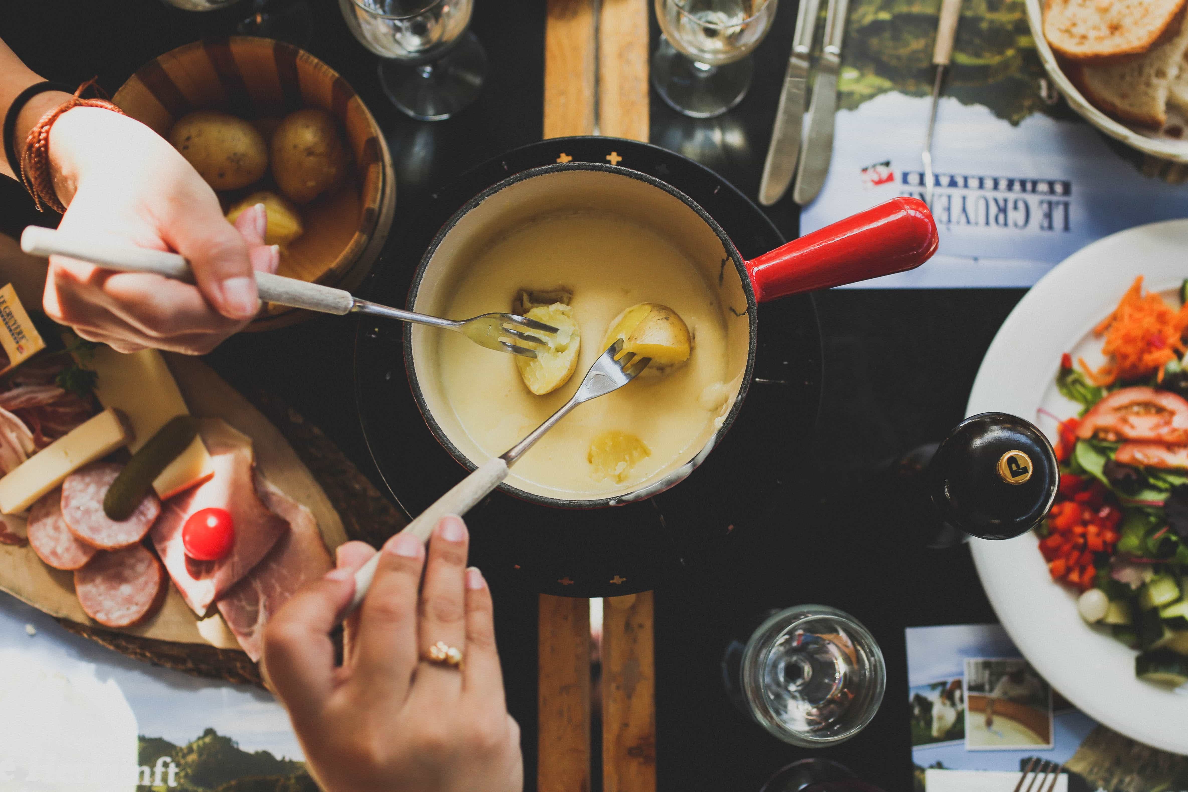 Two hands sharing fondue and potatoes.