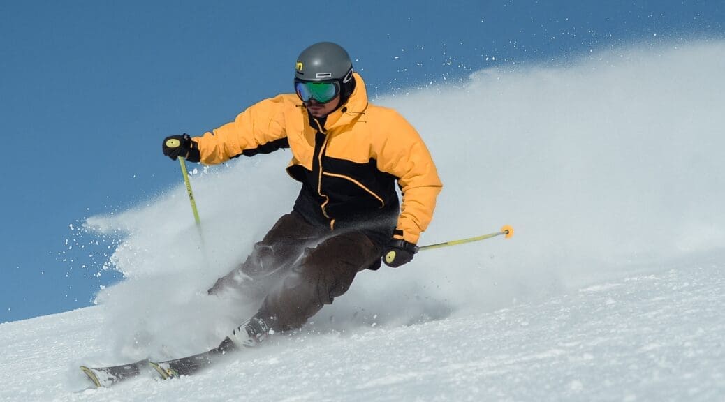 Man skiiing down mountain during ski season, wearing a yellow and black ski jacket