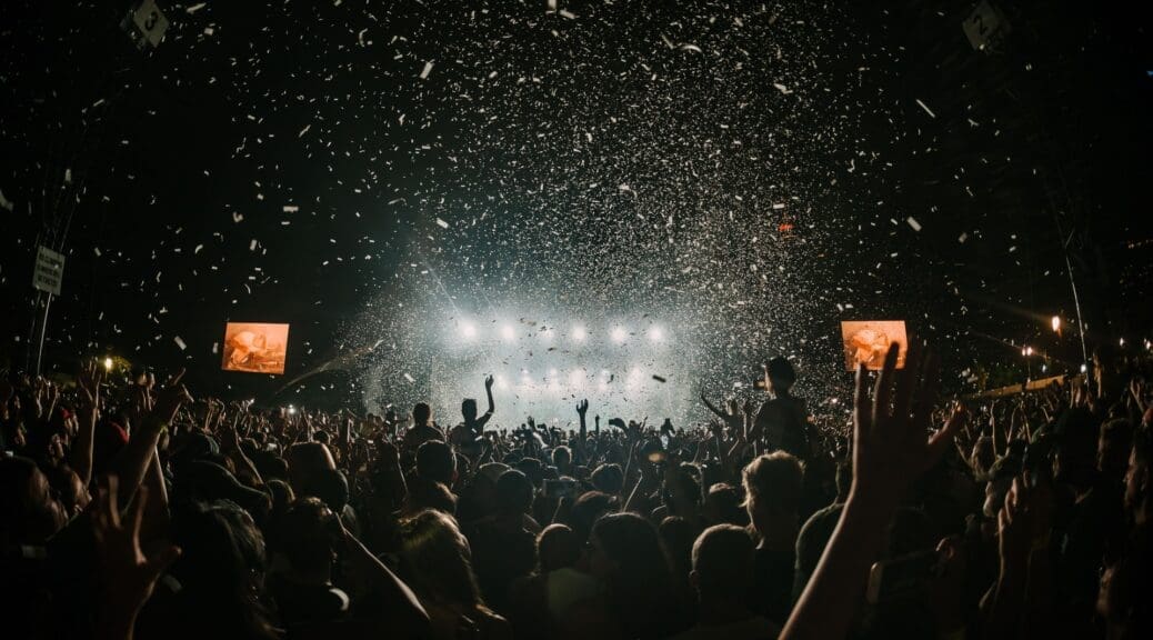 Silhouette of crowds dancing in front of a main stage at a music festival