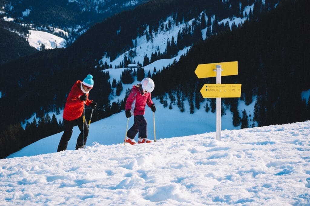 parent and child walking up mountain on skis