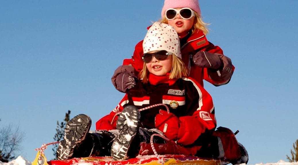 Skiing with kids - children sledding in the Alps