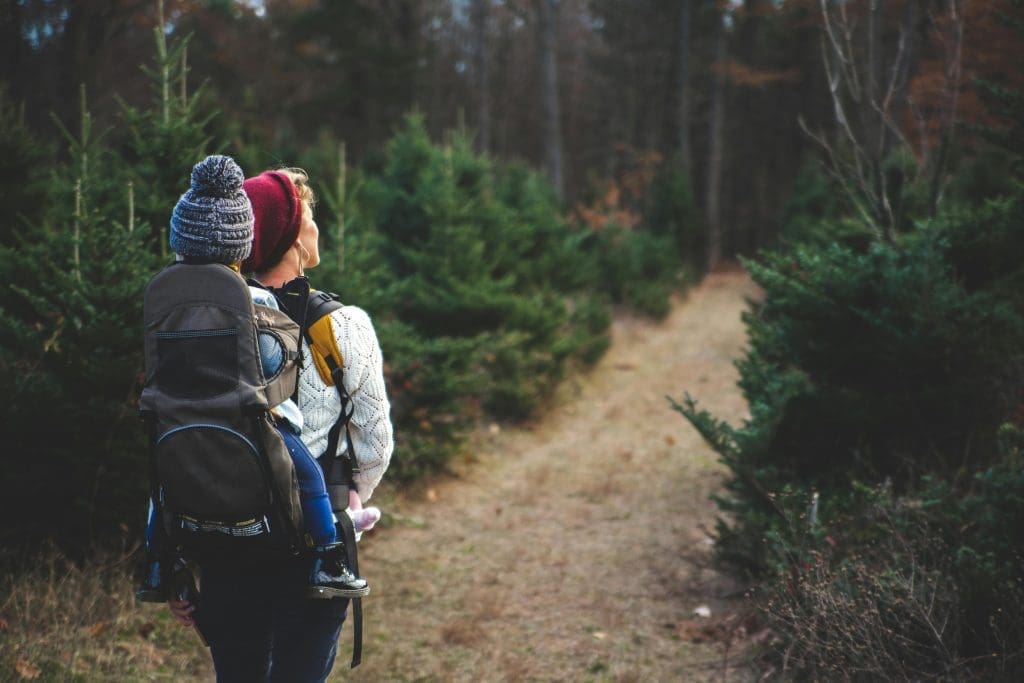 Mother carrying child on her back walking through a forest in the Alps